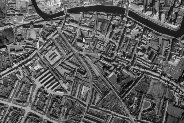 A historic vertical black and white aerial photo of the city of Cork. The city is located along the banks of a river. A cathedral with 3 spires and a star-shaped fort are visible to the left of the image. 