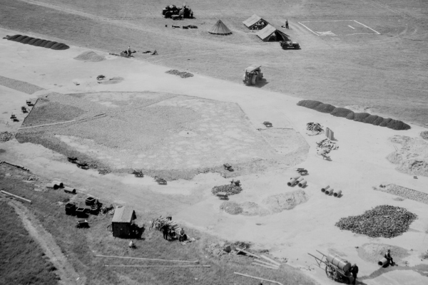 An oblique black and white aerial photo of an airport runway. A large crater in the centre of the runway has been filled in. Works, materials and tents surround the crater.