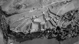 A vertical black and white aerial photo of Stirling Castle, showing fortified buildings on top of a forested ridge.