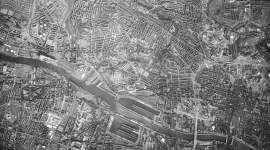 A vertical black and white aerial photo of the city of Glasgow. The river Clyde is visible at the bottom of the image, with clear grids of streets above.