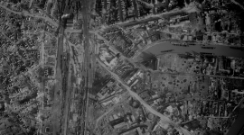 A historic black and white vertical aerial photo of a bombed city. Numerous roofless houses and craters are visible. To the left of the image are trains in some railway sidings. To the right are boats on a canal.